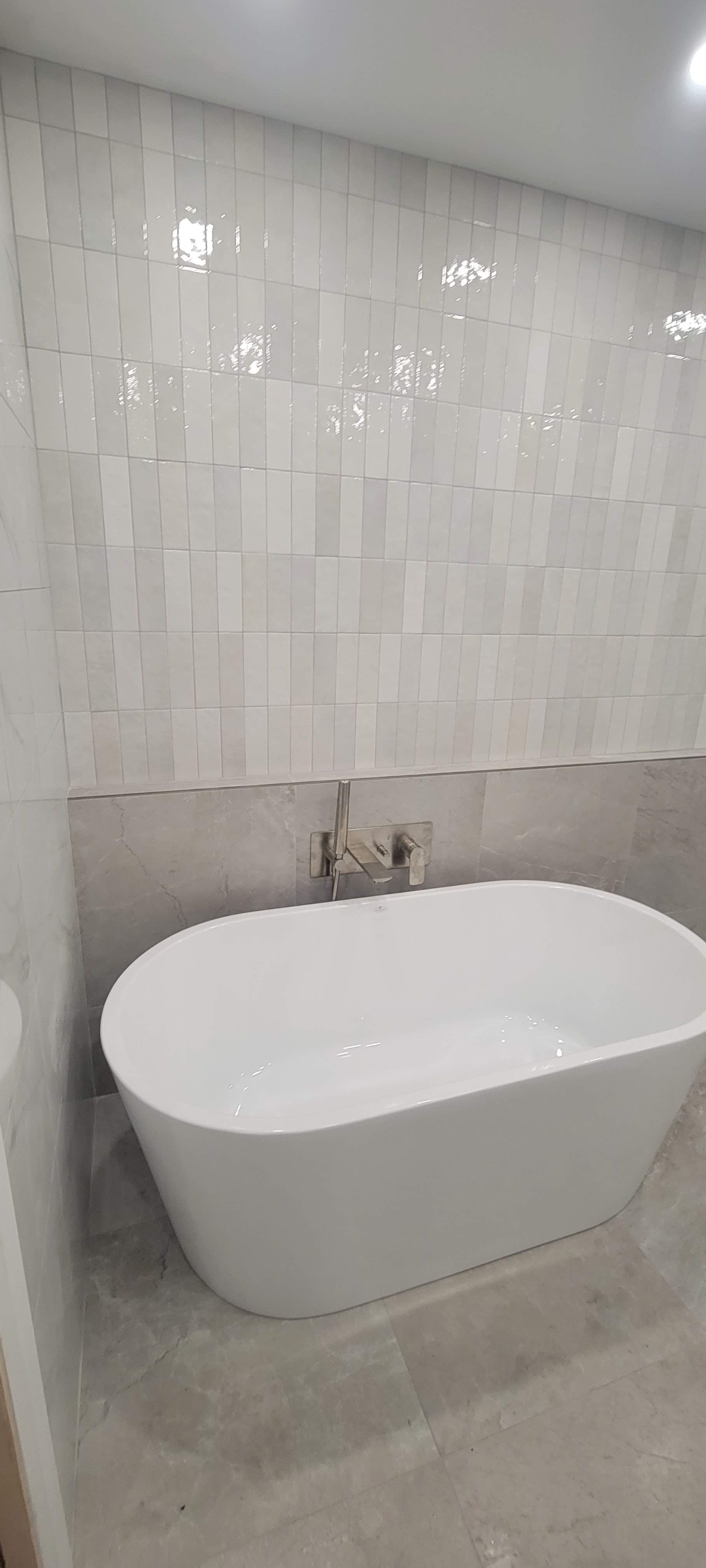 Il y a une baignoire dans la salle de bain avec du carrelage blanc au mur.