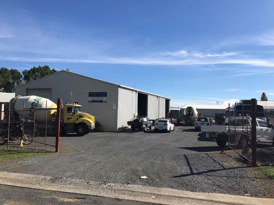 A Gravel Lot with A Gray Warehouse and Several Trucks on A Sunny Day — Haigh Truck & 4WD Repairs In Orange, NSW