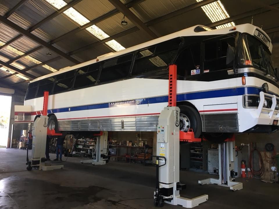 Bus raised on a lift in a garage, white with blue and red stripes.