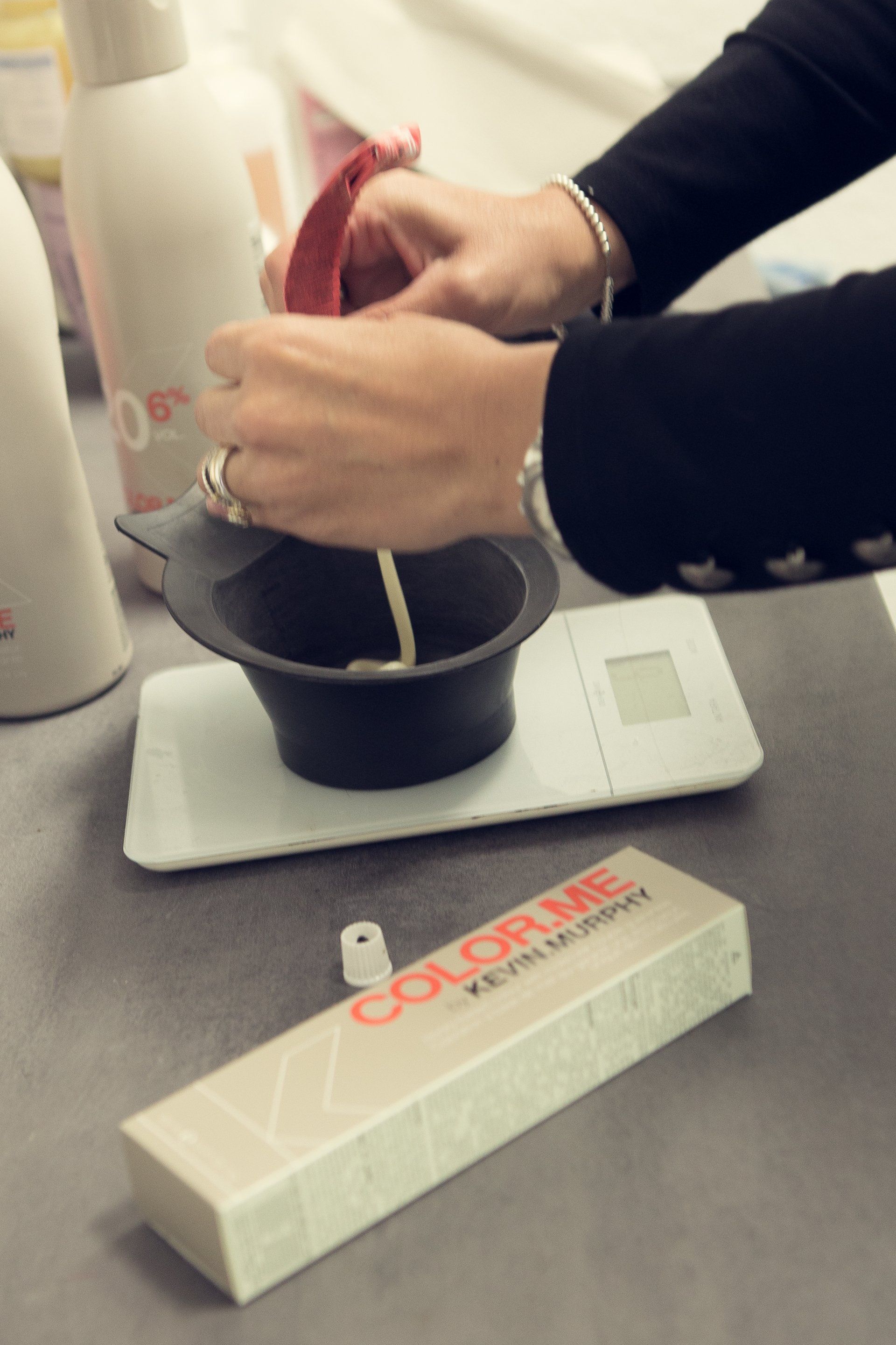Eine Frau mischt Haarfärbemittel in einer Schüssel neben einer Schachtel mit der Aufschrift „Color Me“