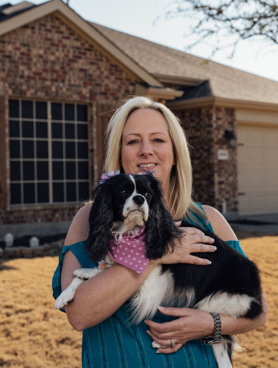 A woman is holding a black and white dog in front of a house.