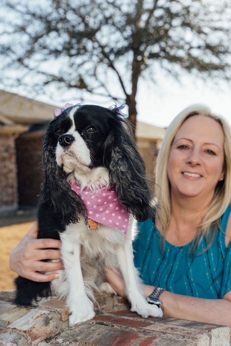 A woman is holding a black and white dog wearing a pink bandana.