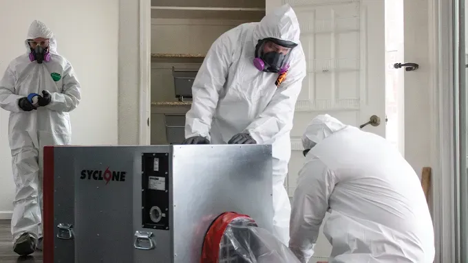 A man wearing a hard hat and goggles is standing in a room.