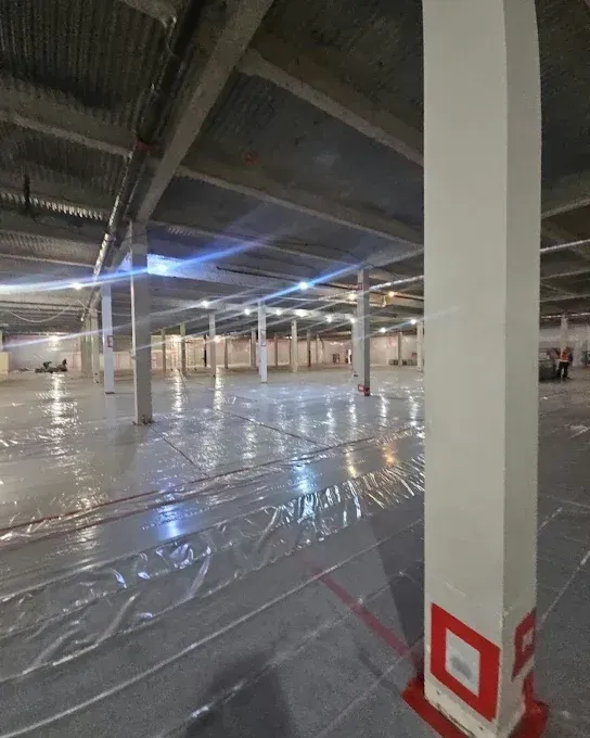 Large empty warehouse interior with white support columns and plastic sheeting on the floor.
