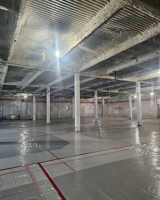 Empty warehouse interior with concrete floor, white columns, exposed ceiling, and red taped lines.