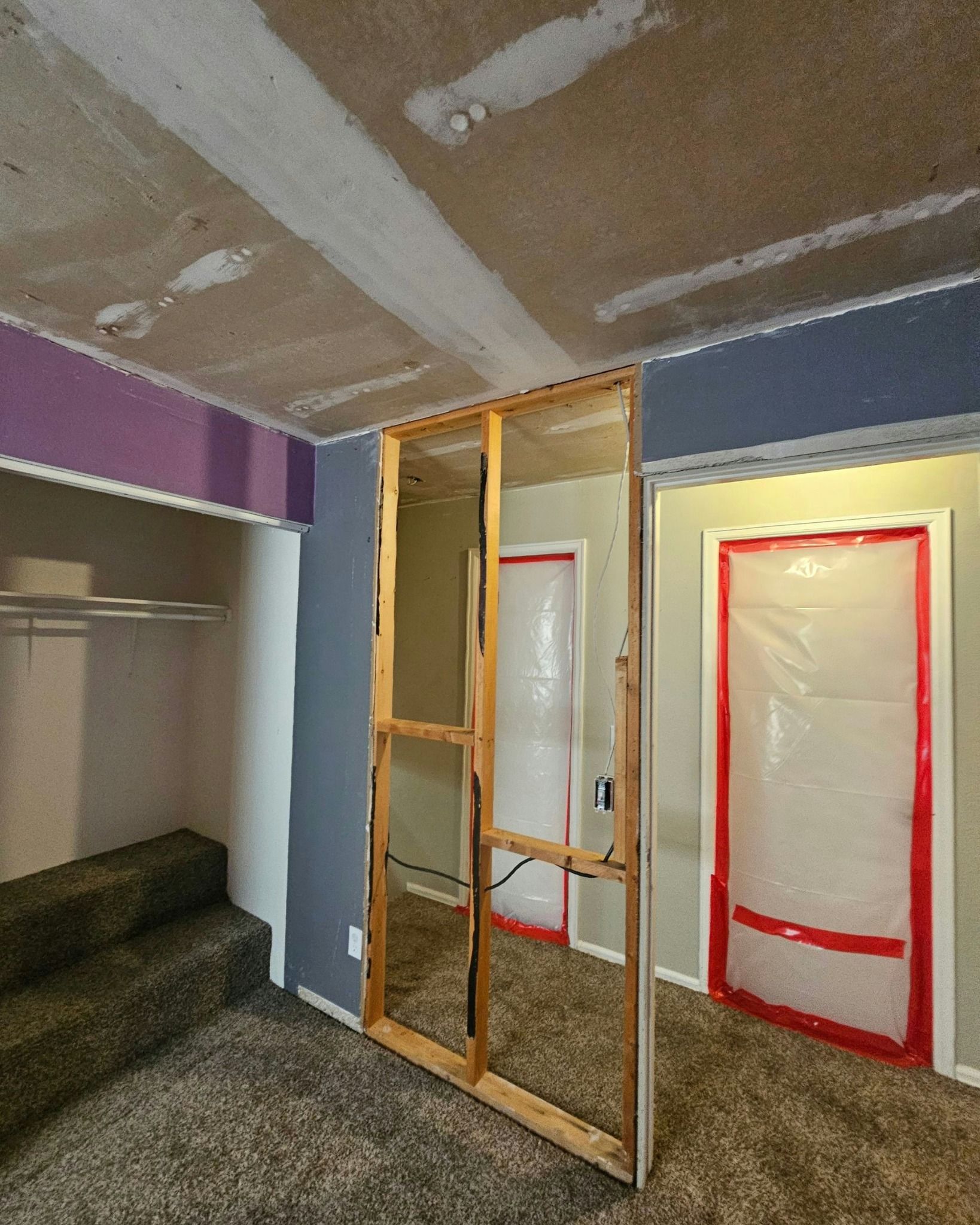 Room with unfinished walls, exposed framing, two doorways covered in plastic, and closet.