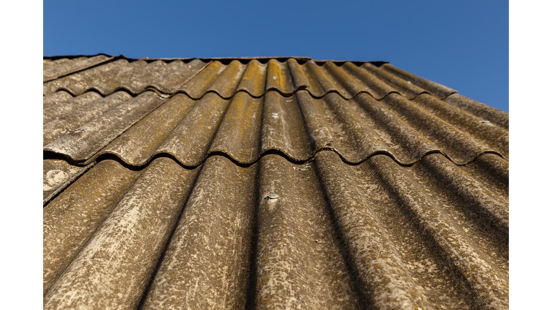 Close-up of an old, weathered, corrugated roof against a clear blue sky.