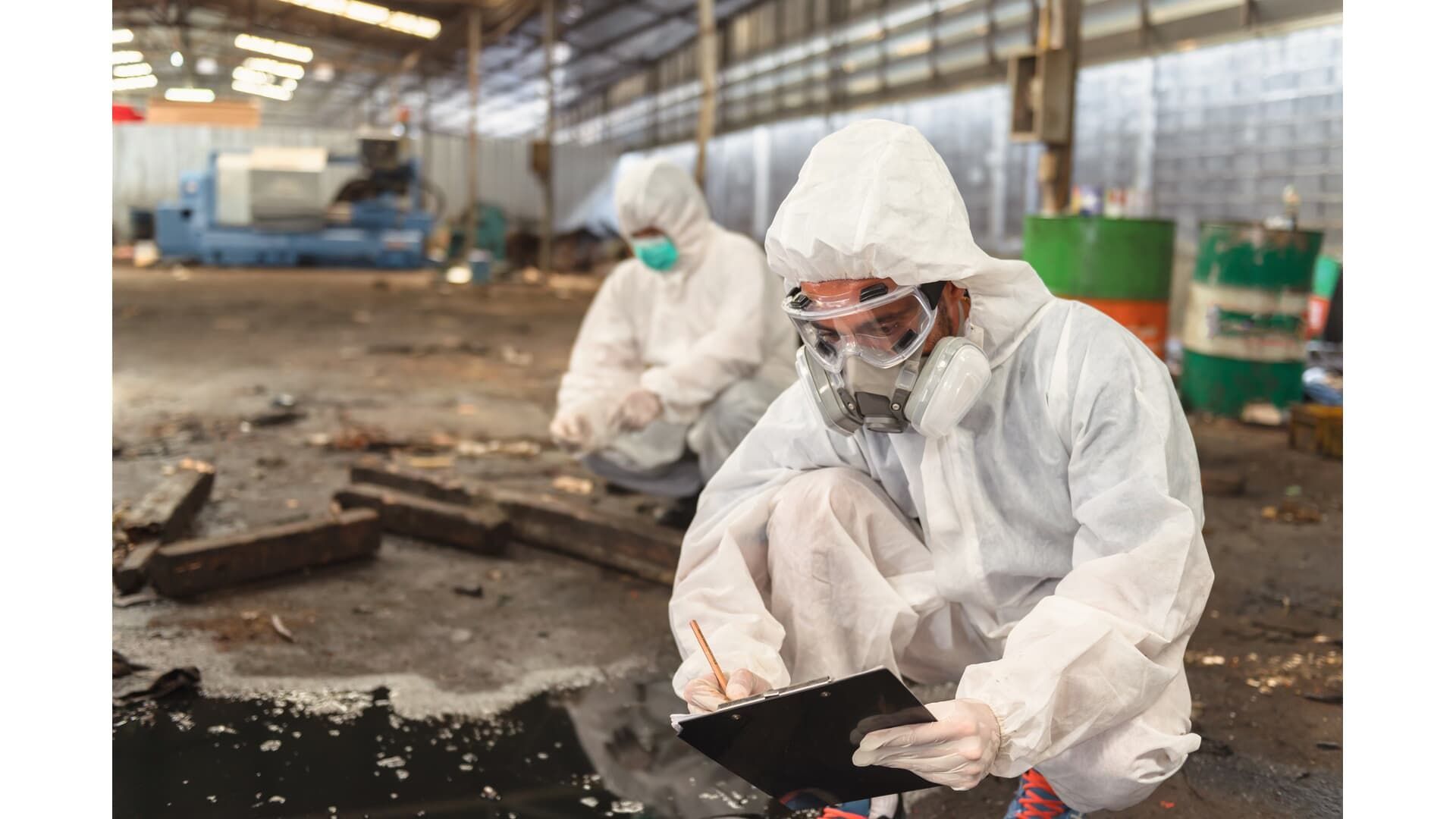 Two workers in hazmat suits inspect a contaminated industrial site.