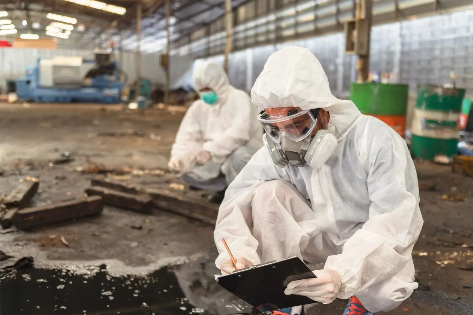 Two people in hazmat suits inspecting a flooded industrial site.