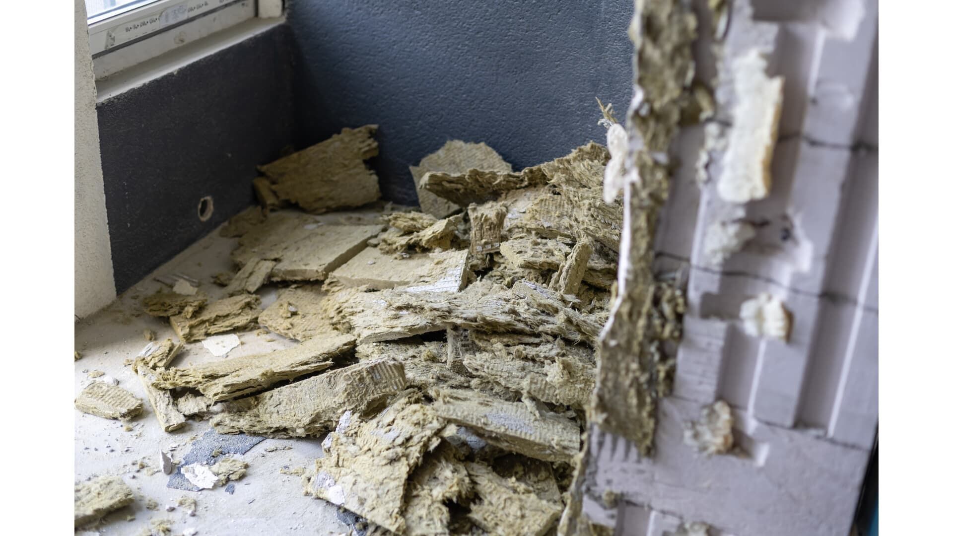 Pile of damaged wallboard and insulation debris on a room floor, near a window.