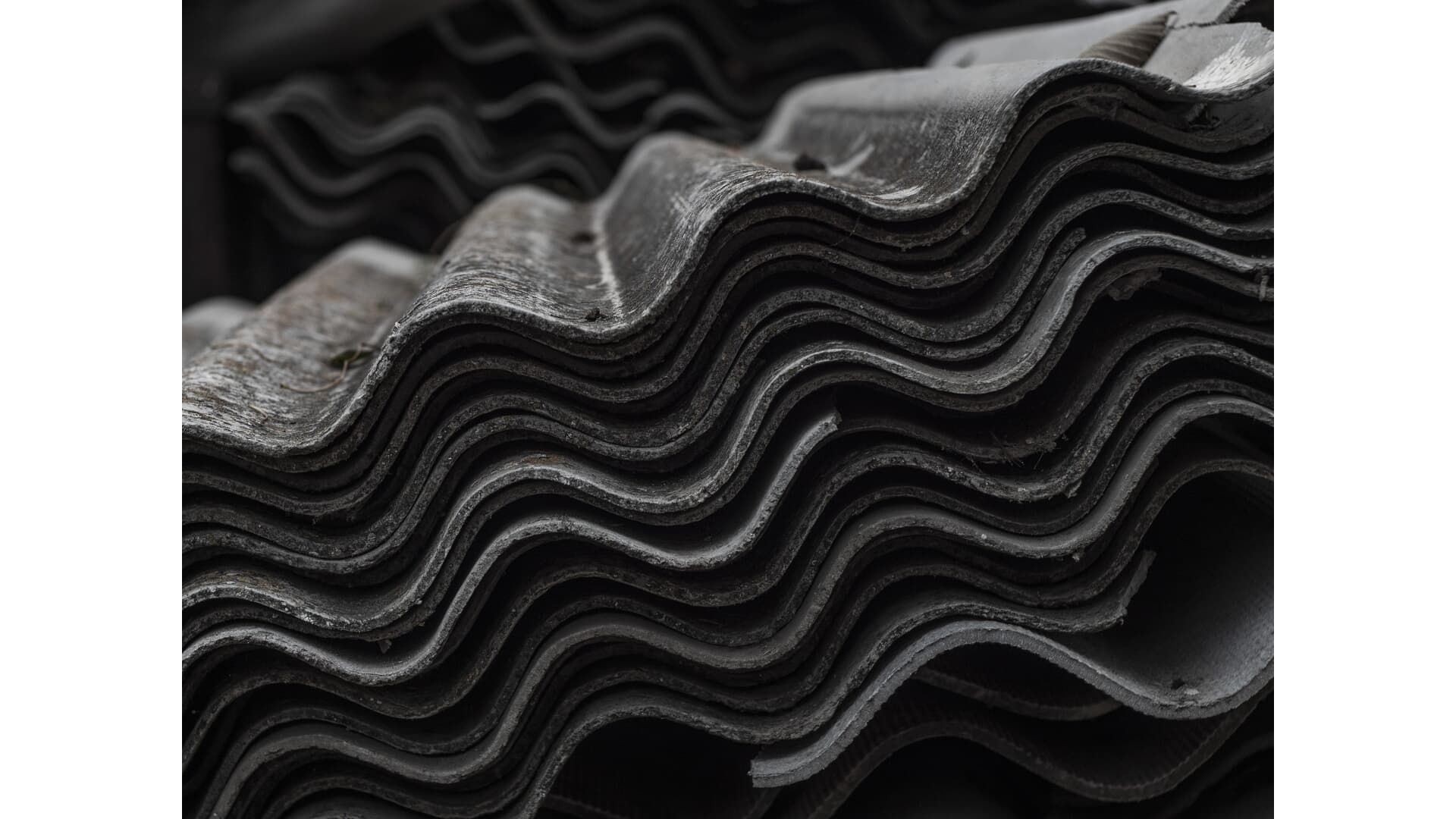 Stack of corrugated, gray asbestos roofing tiles.