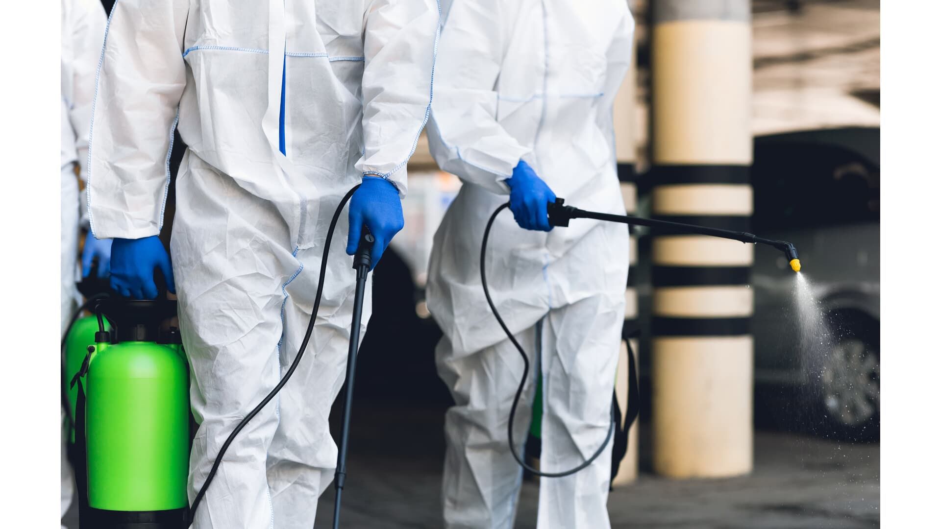 People in protective suits spraying disinfectant in a parking garage.