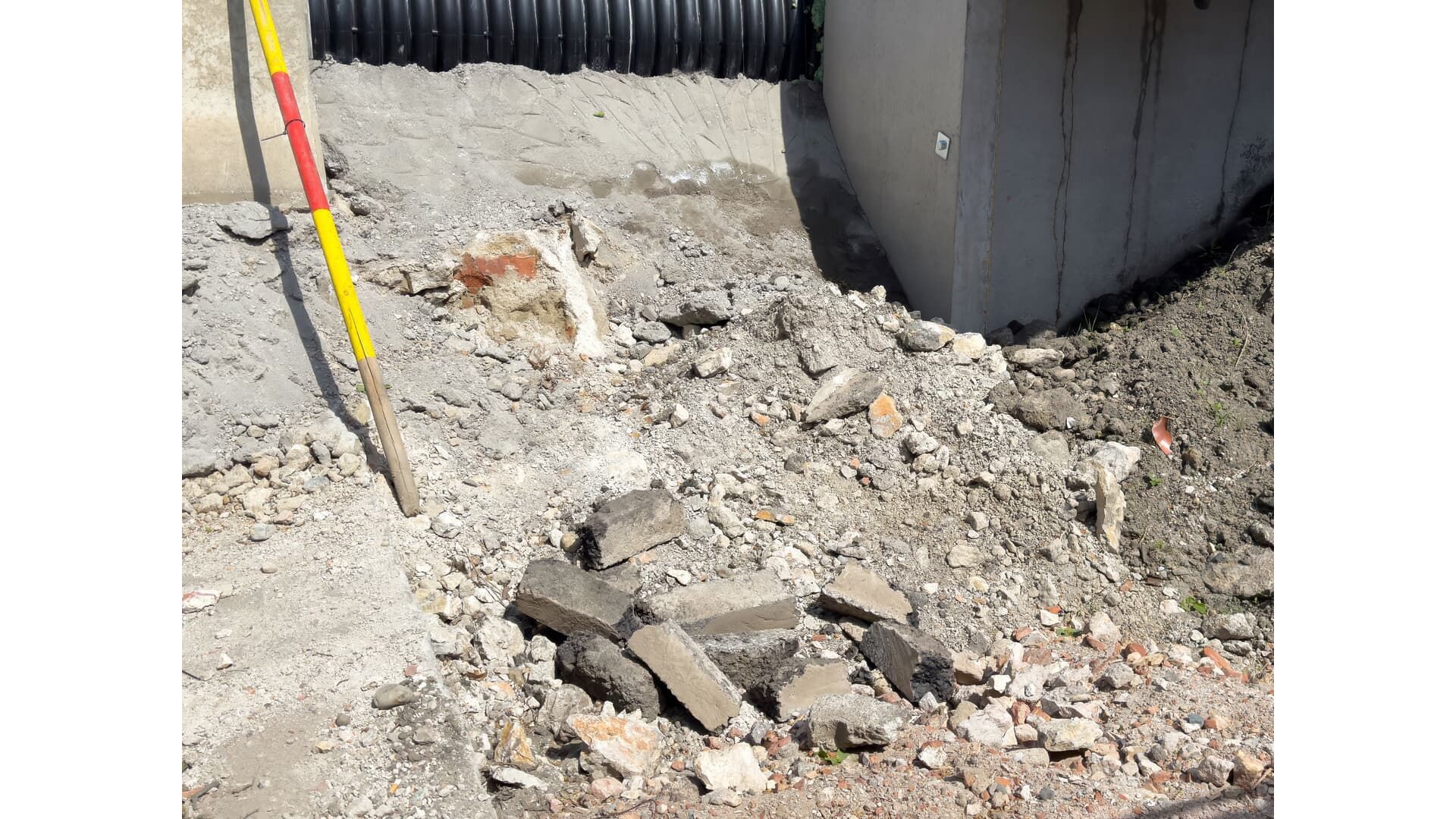Construction site with concrete debris, black pipe, and survey rod.