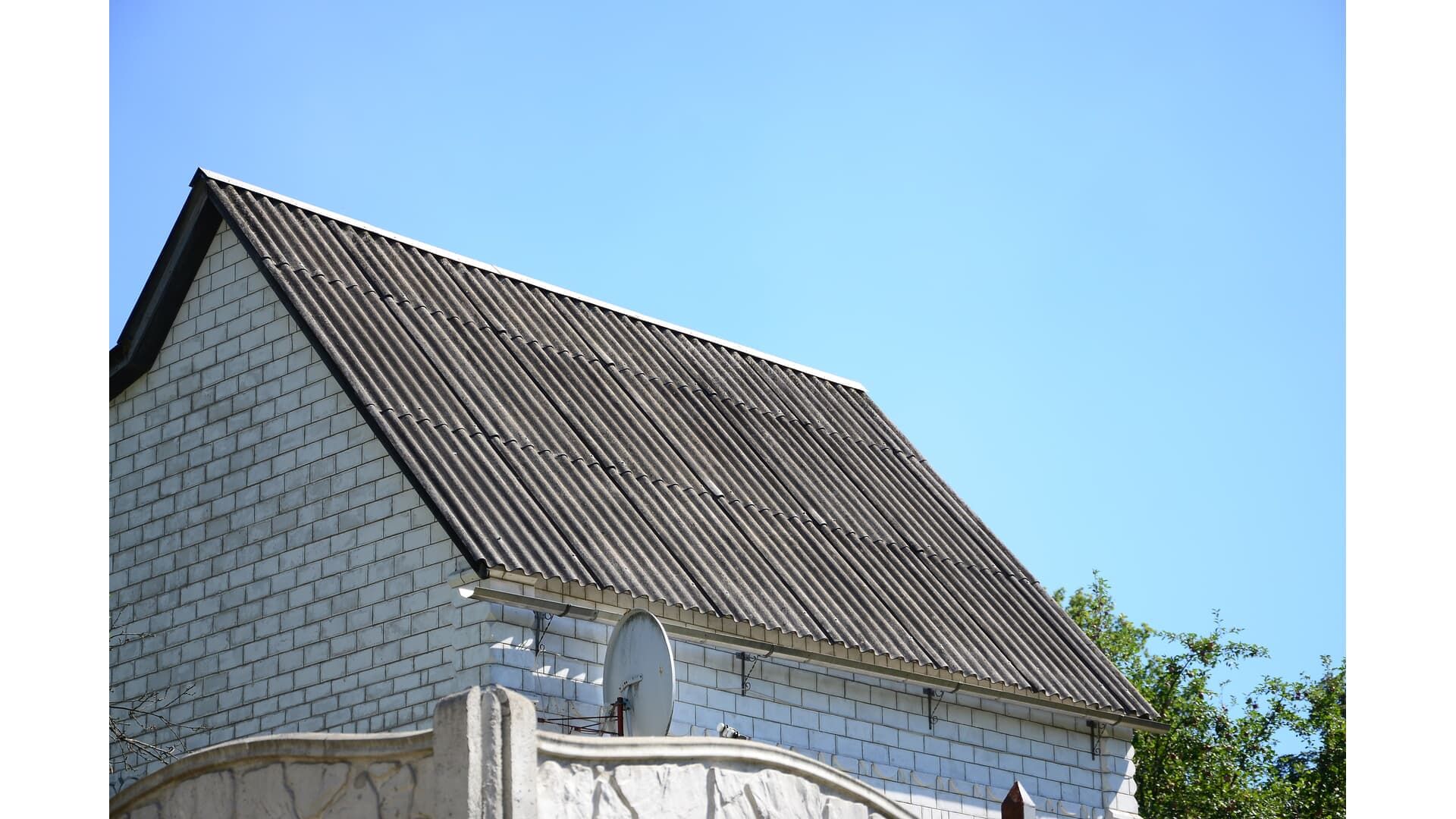White brick building with a gray corrugated roof, against a clear blue sky.