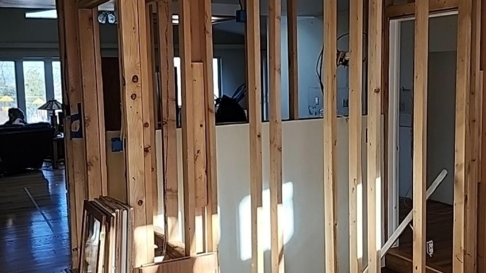 Wooden frame wall construction; interior view of a building under renovation. Sunlight streams through the vertical beams.