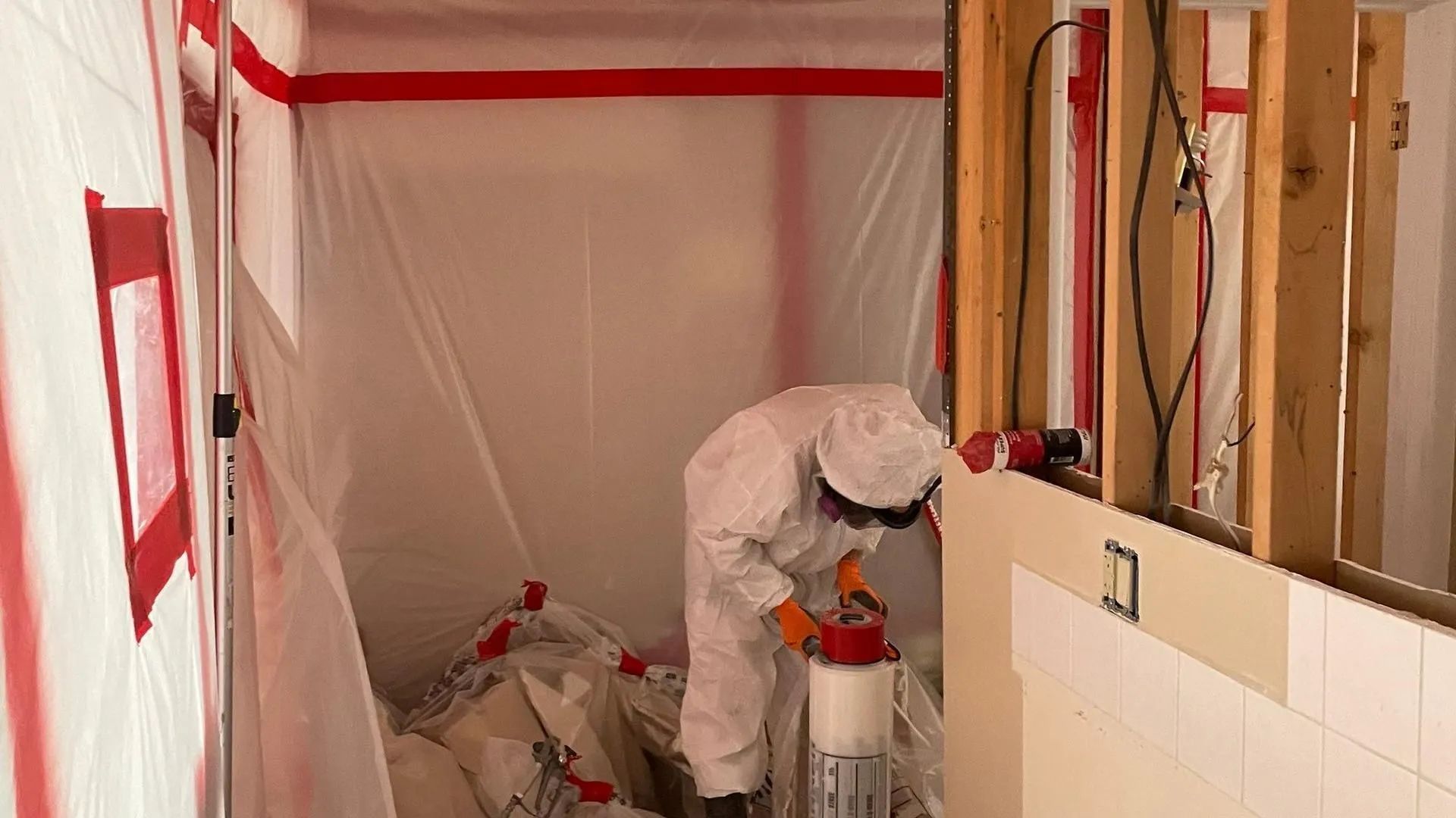 Person in white protective suit inside a containment area, working on a wall with equipment.