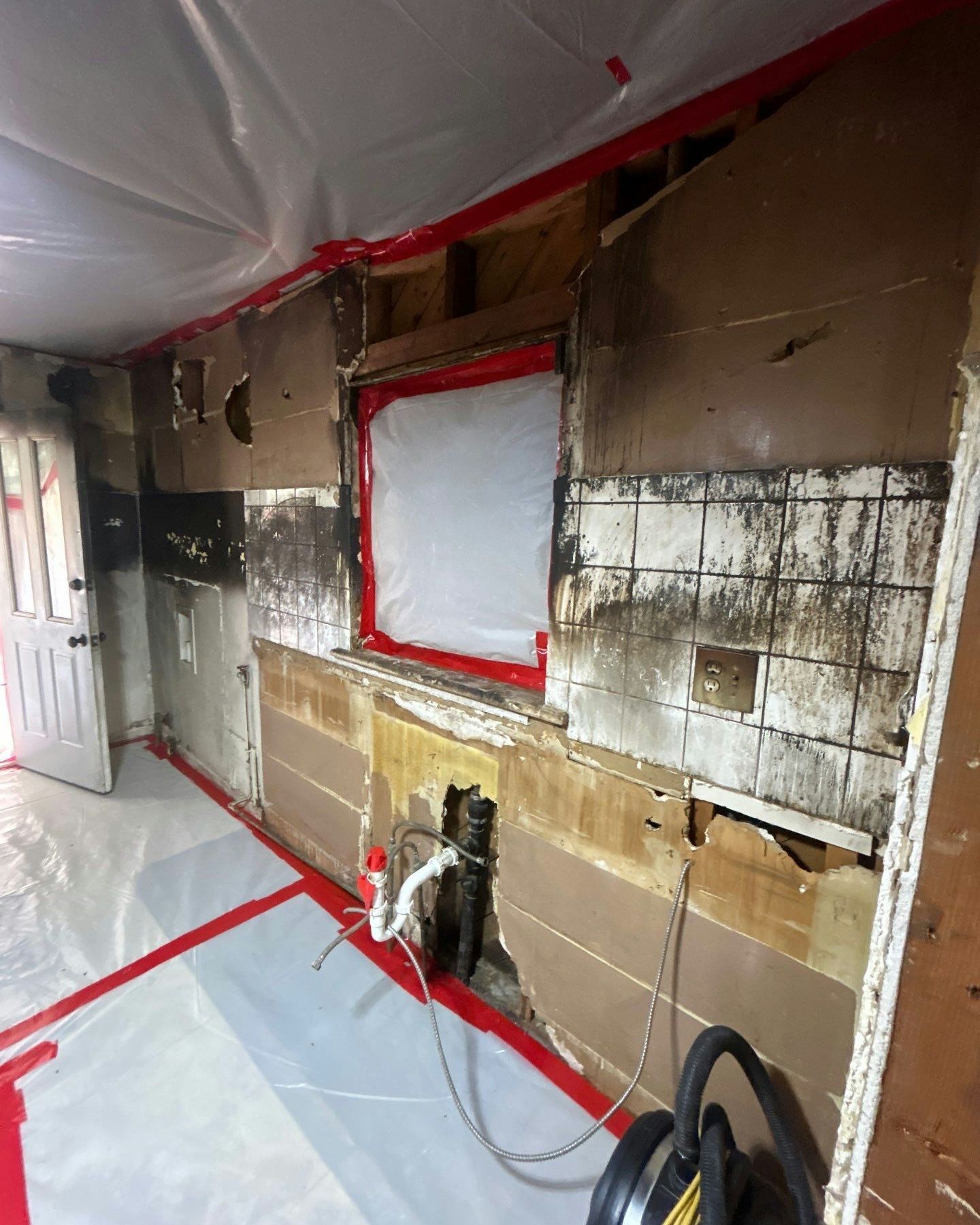 Fire-damaged kitchen interior with peeling walls and protective sheeting. Black soot, exposed framing, and red tape visible.