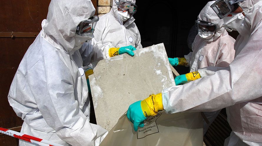 People in protective suits handling a concrete slab near a garage.