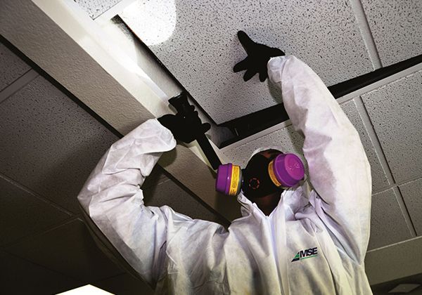 Person in protective suit and respirator removes ceiling tile.