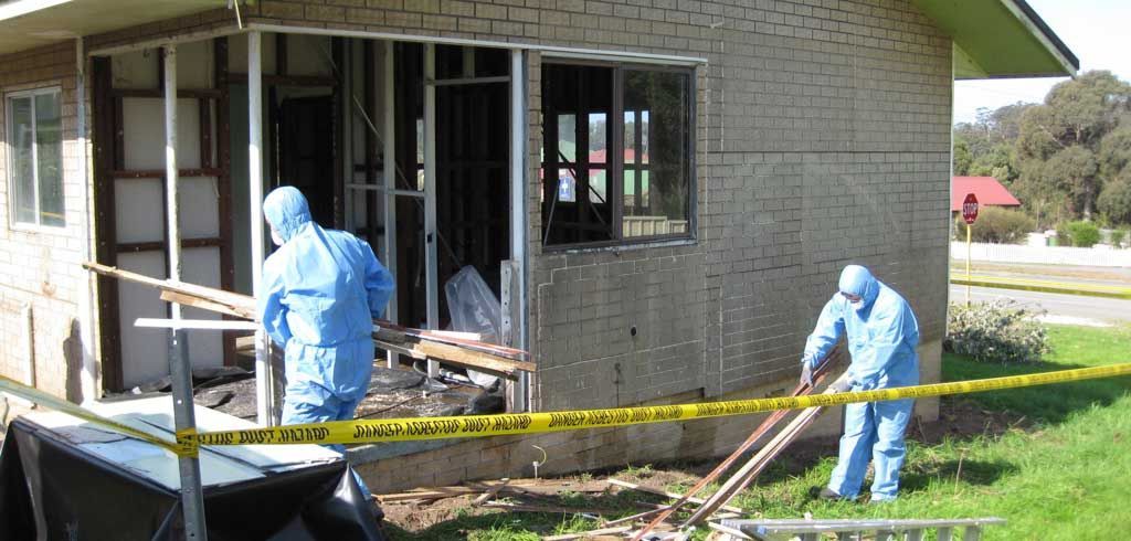 Ceiling damage in a room with furniture covered in plastic, and buckets on the floor.
