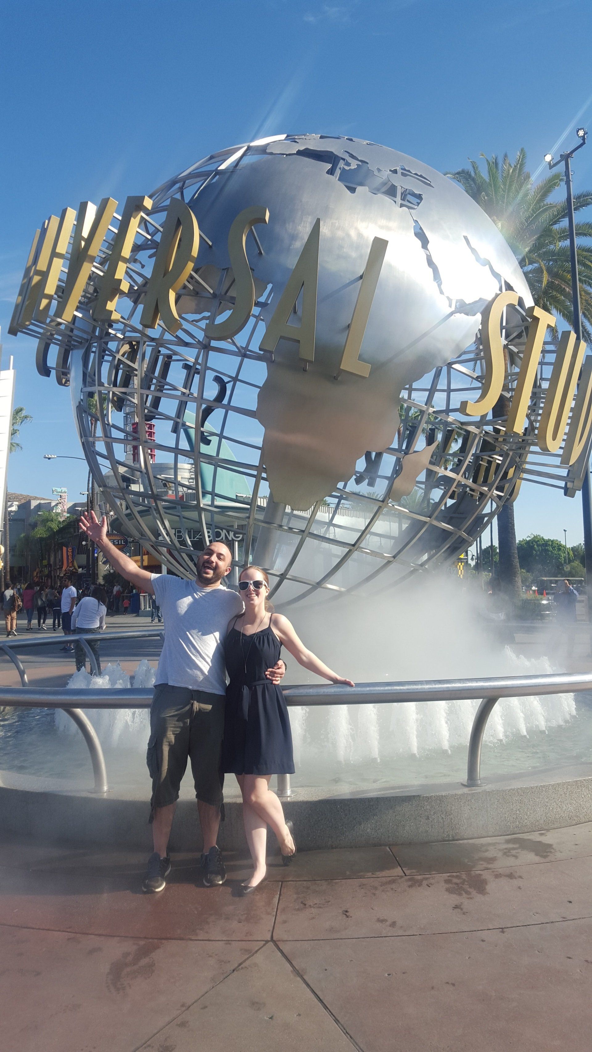 A man and a woman are posing for a picture in front of the universal studios globe.