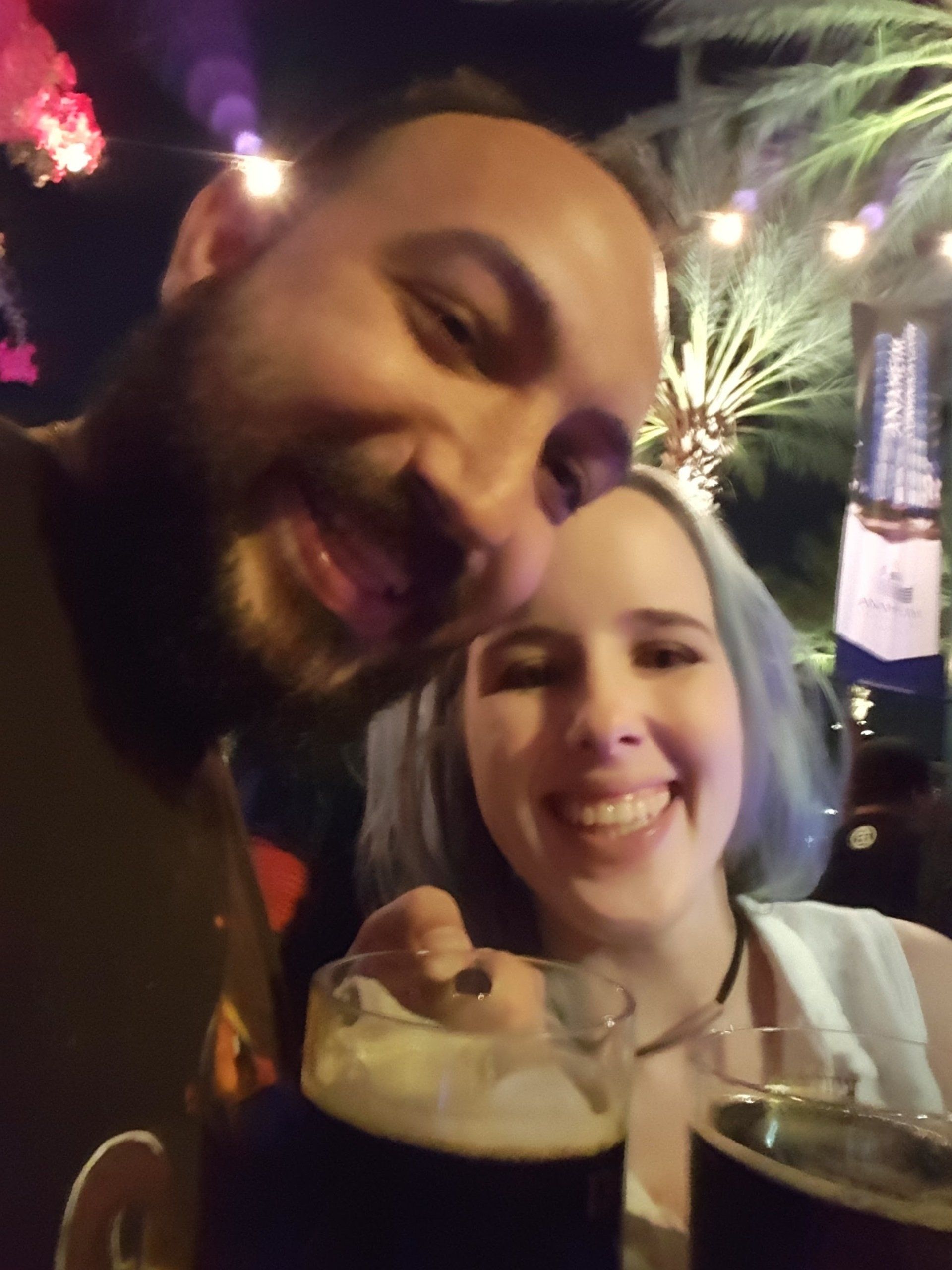 A man and a woman are posing for a picture while drinking beer