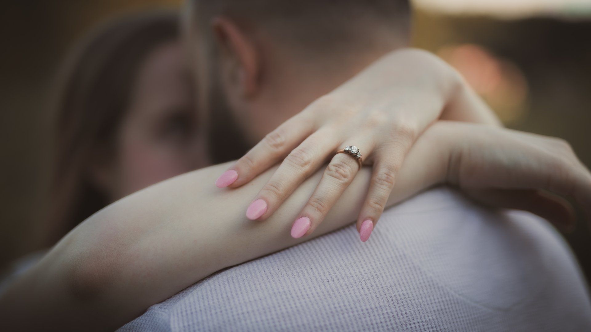A woman with a ring on her finger is hugging a man.