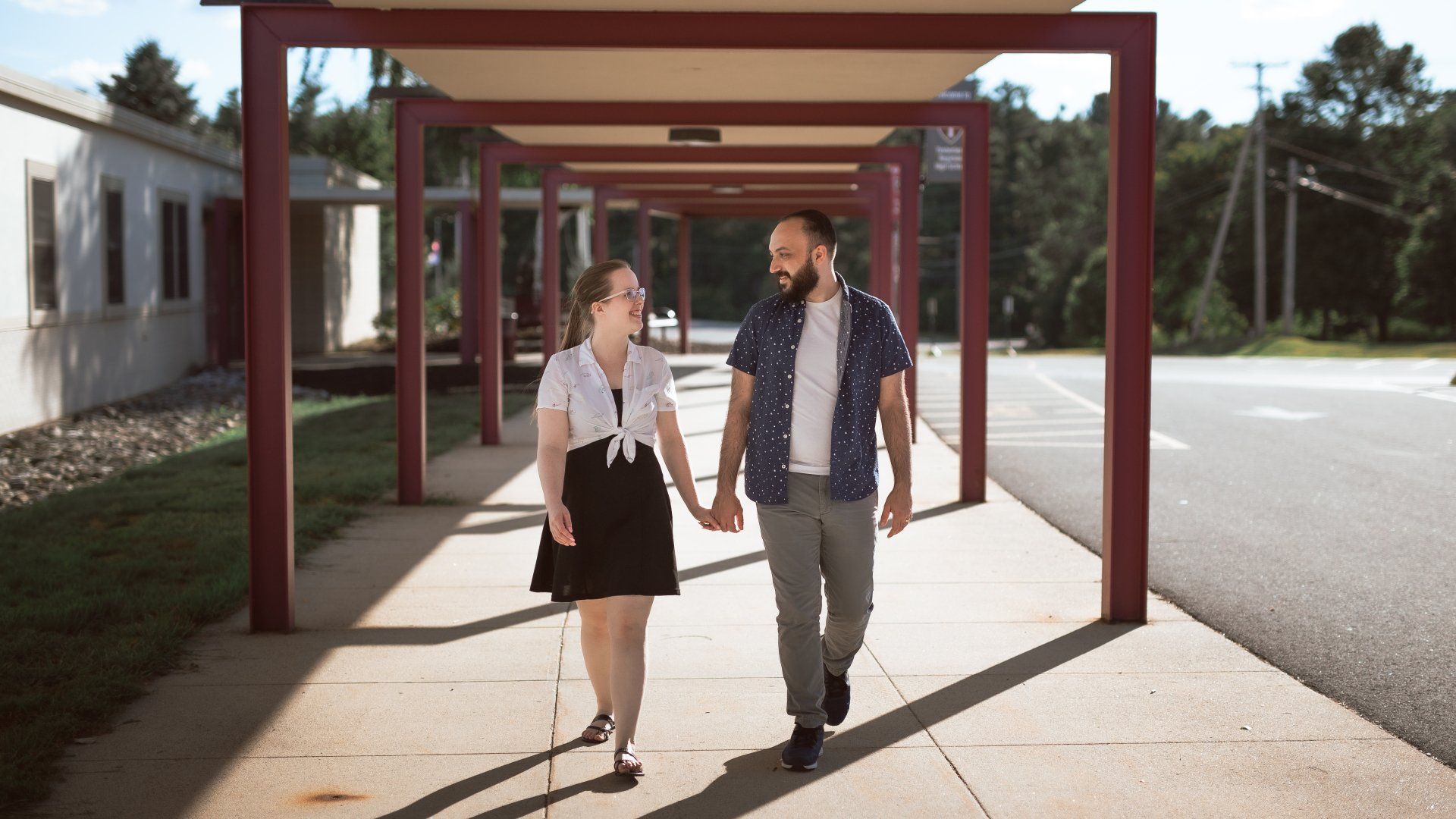 A man and a woman are walking down a sidewalk holding hands.