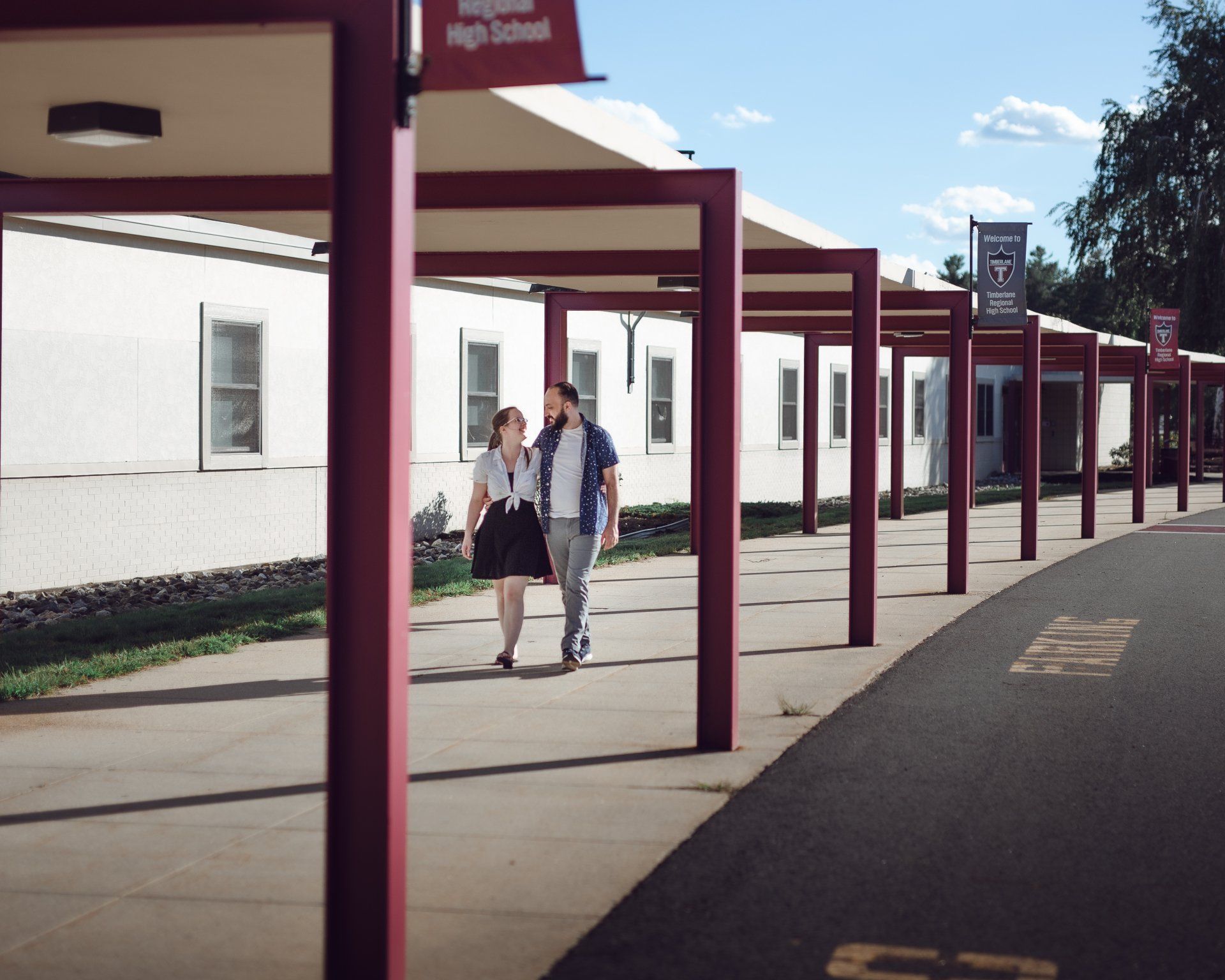 A man and woman are walking down a sidewalk in front of a high school