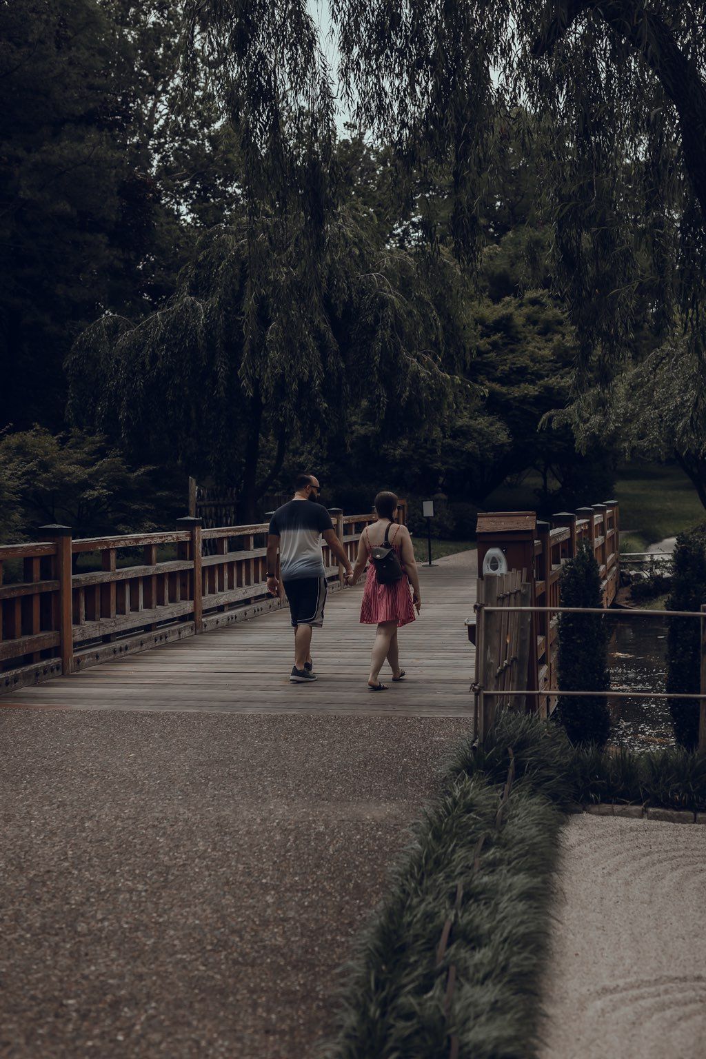 A man and a woman are walking across a bridge in a park.