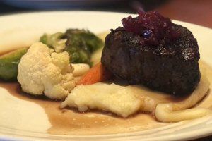 A close up of a plate of food with meat and vegetables on a table.