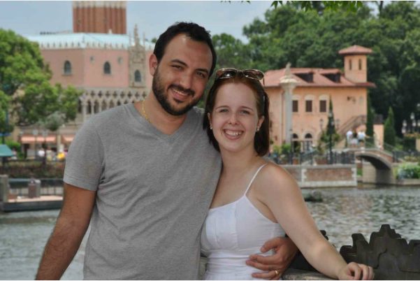 A man and a woman are posing for a picture with a building in the background