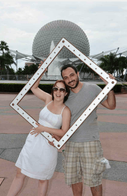 A man and a woman are holding a picture frame in front of a fountain.
