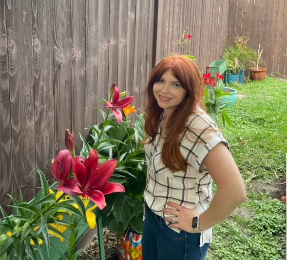 Woman with red hair and plaid shirt near blooming lilies in a garden.