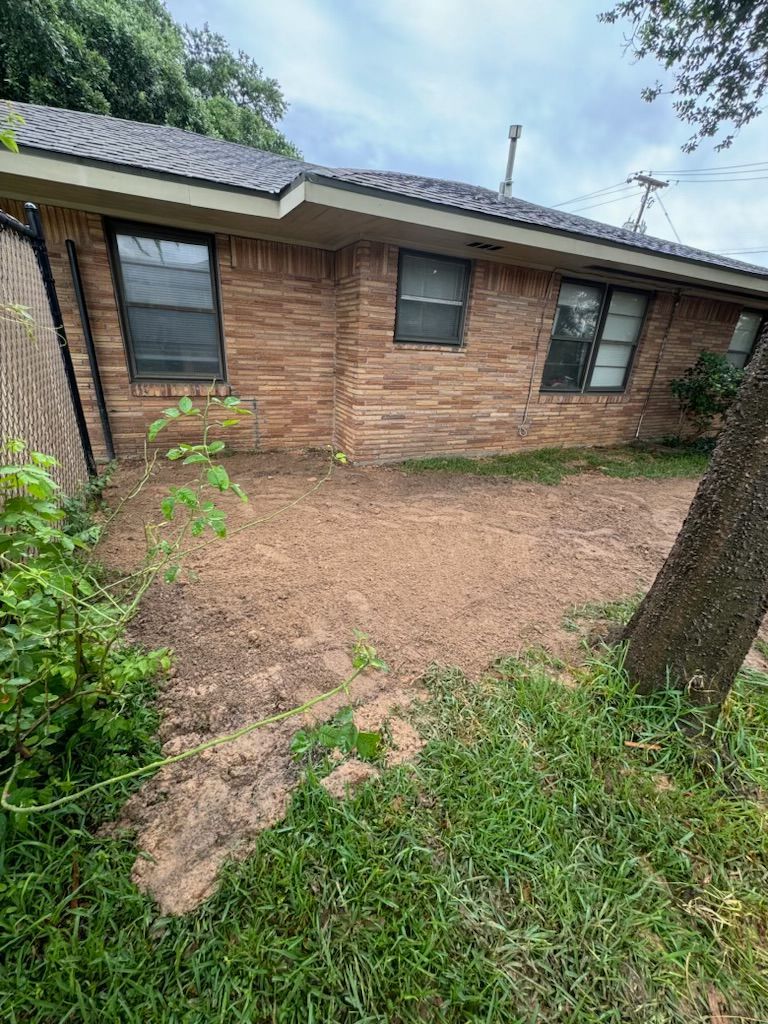 Brick house exterior with three windows. Dirt and grass area in the yard.