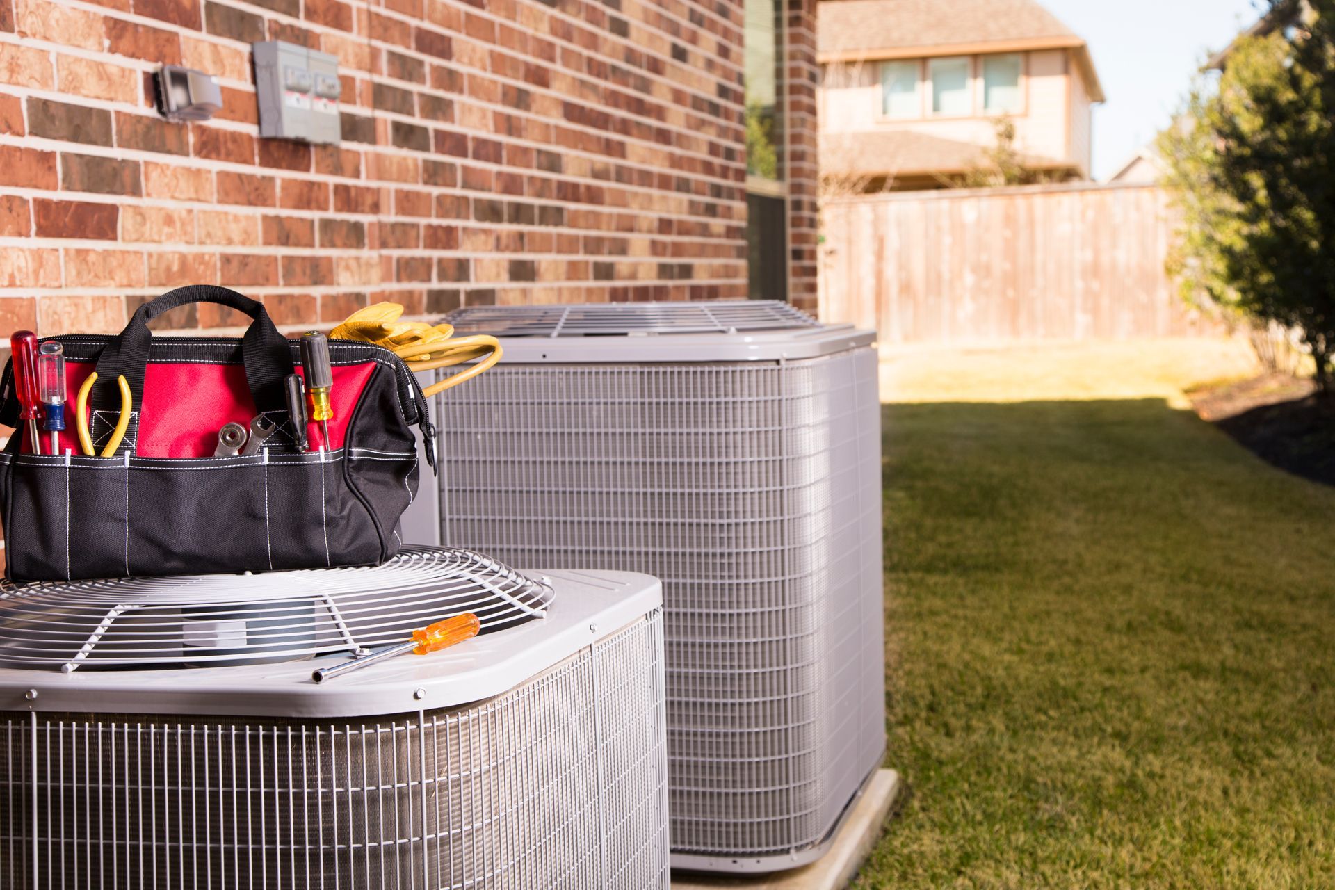 Two air conditioners are sitting next to each other on the side of a brick building.