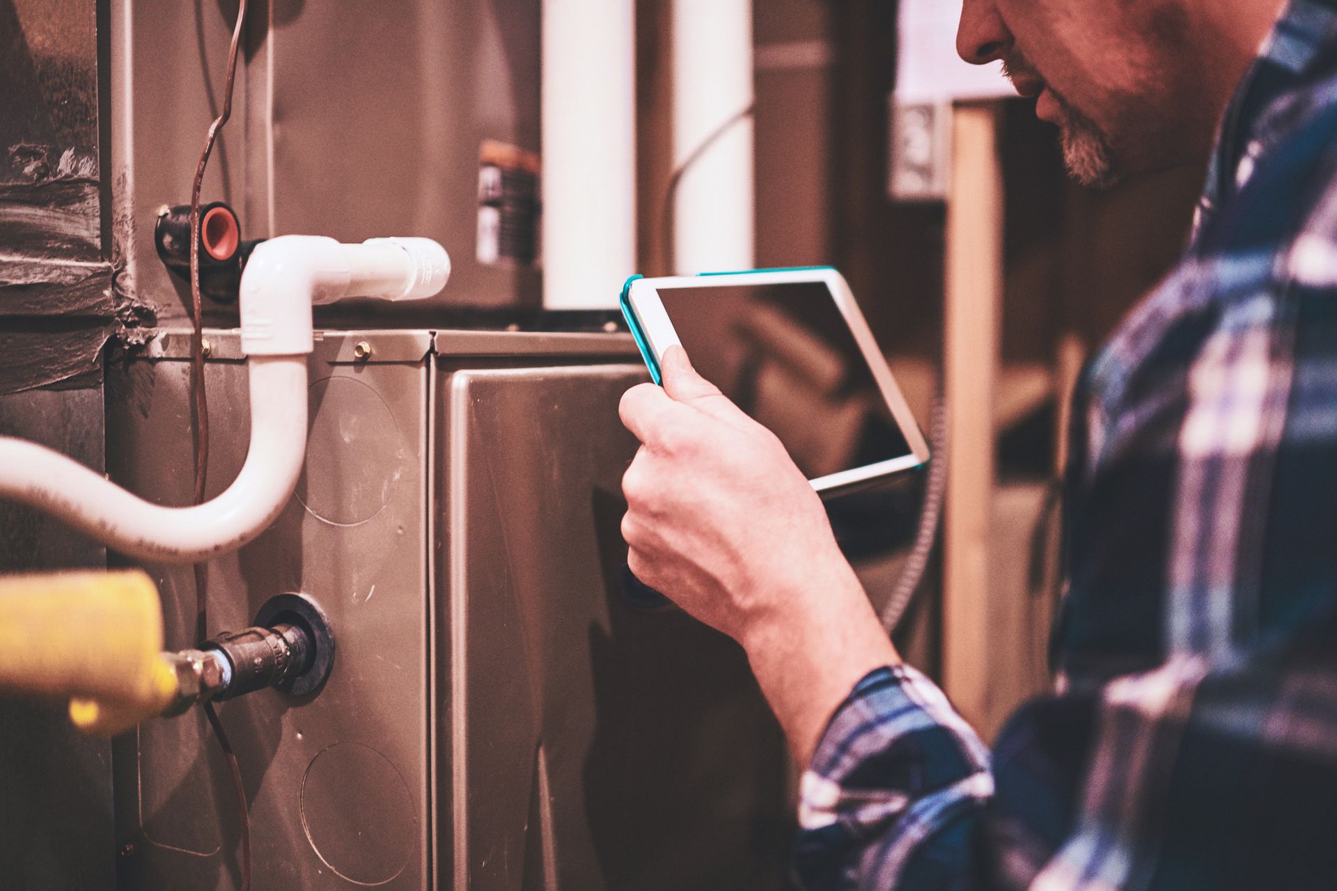 A man is looking at a tablet while working on a heating system.