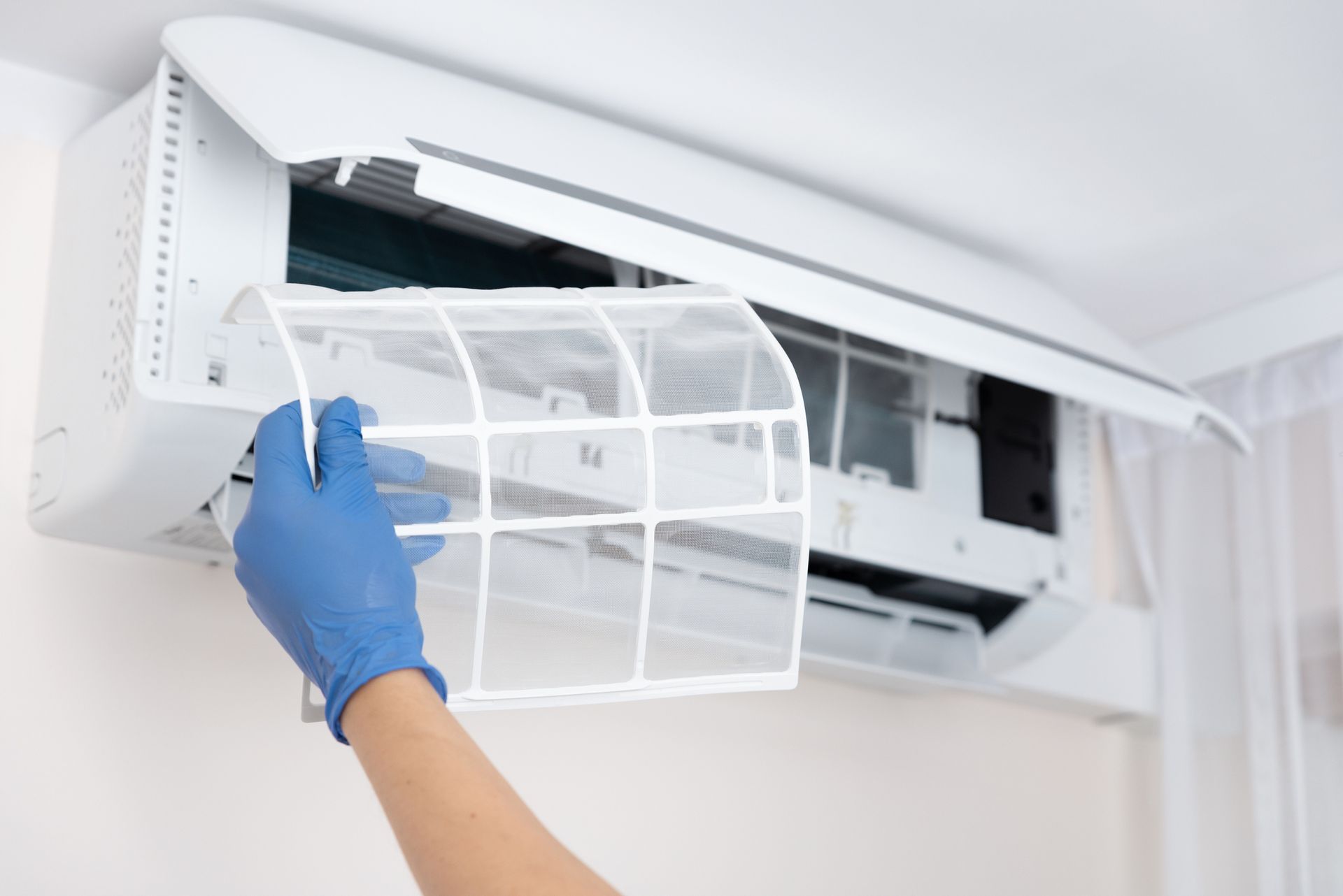 A person wearing blue gloves is cleaning an air conditioner.