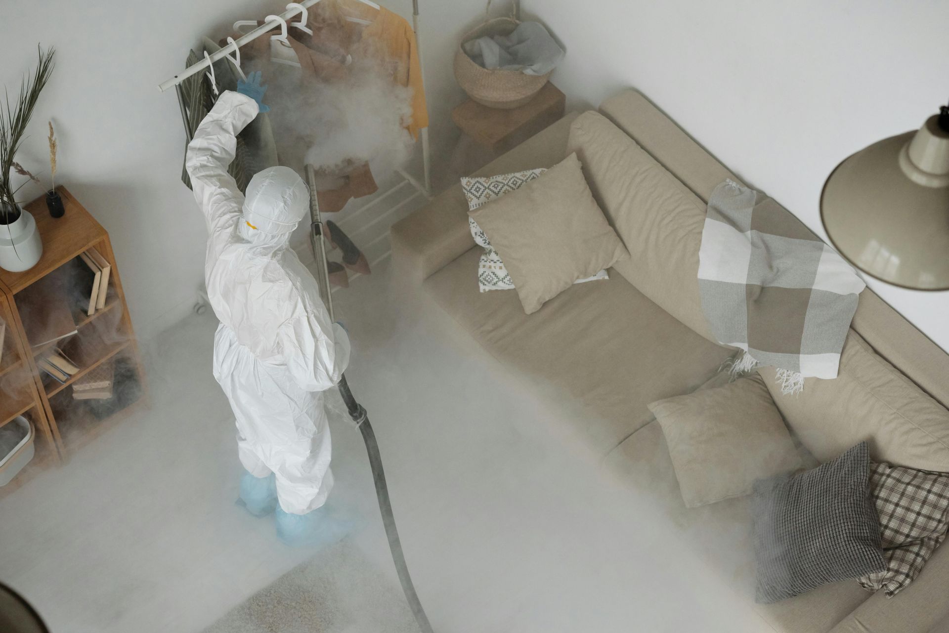 A person in a protective suit is disinfecting a living room.