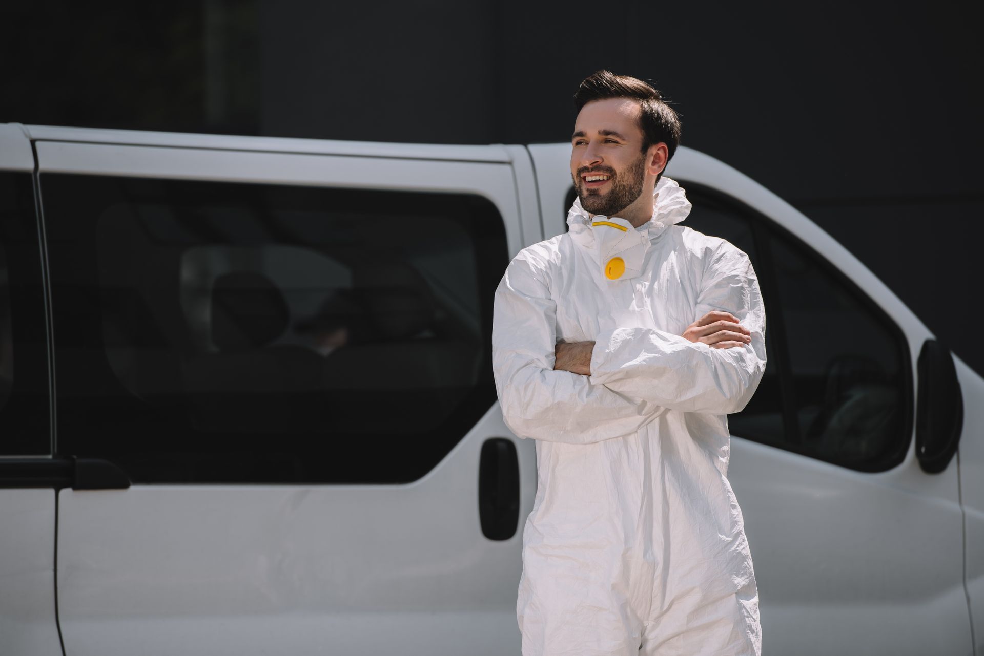 A man in a protective suit is standing in front of a white van with his arms crossed.