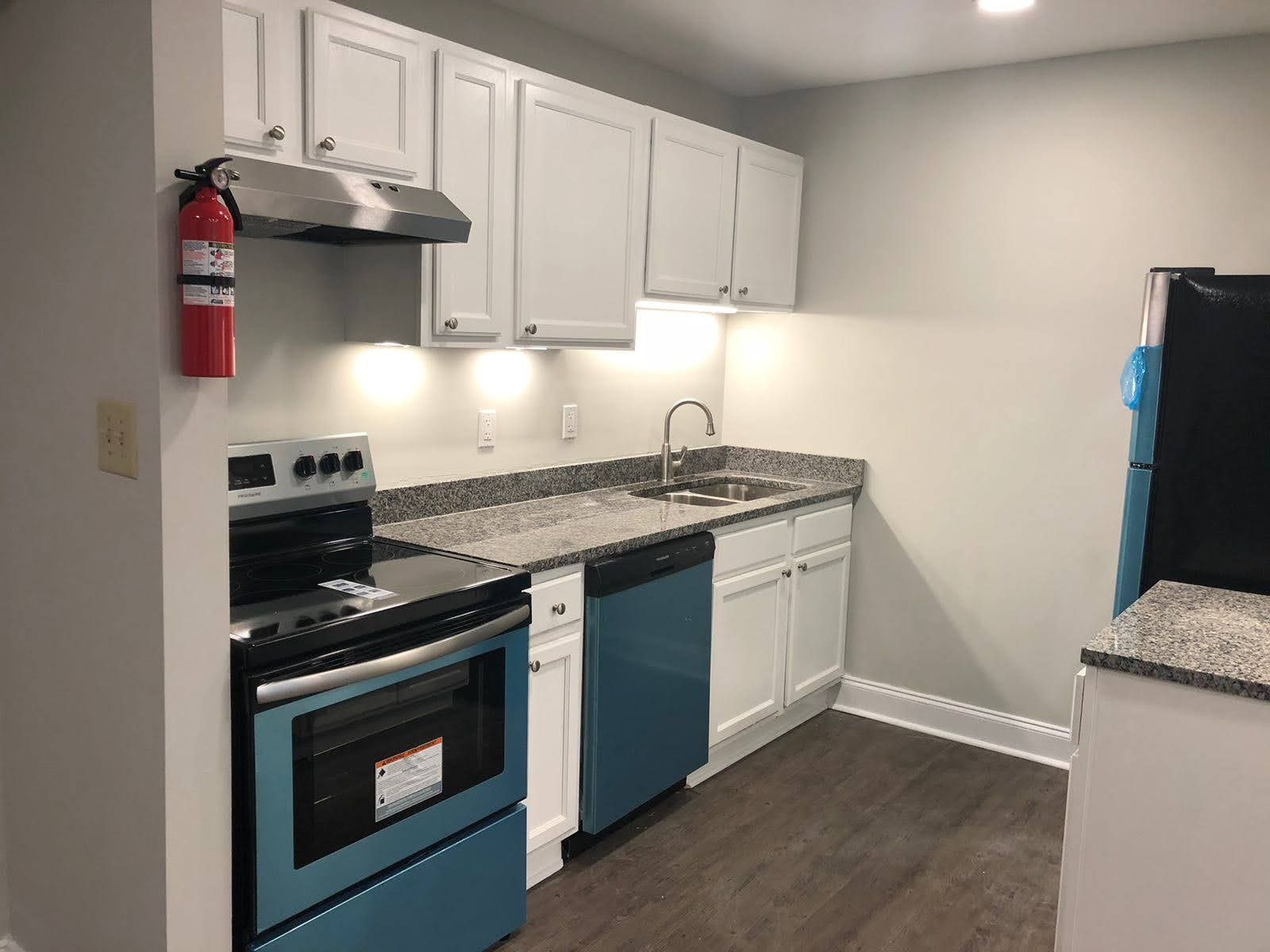 A kitchen with white cabinets and blue appliances and a fire extinguisher on the wall.
