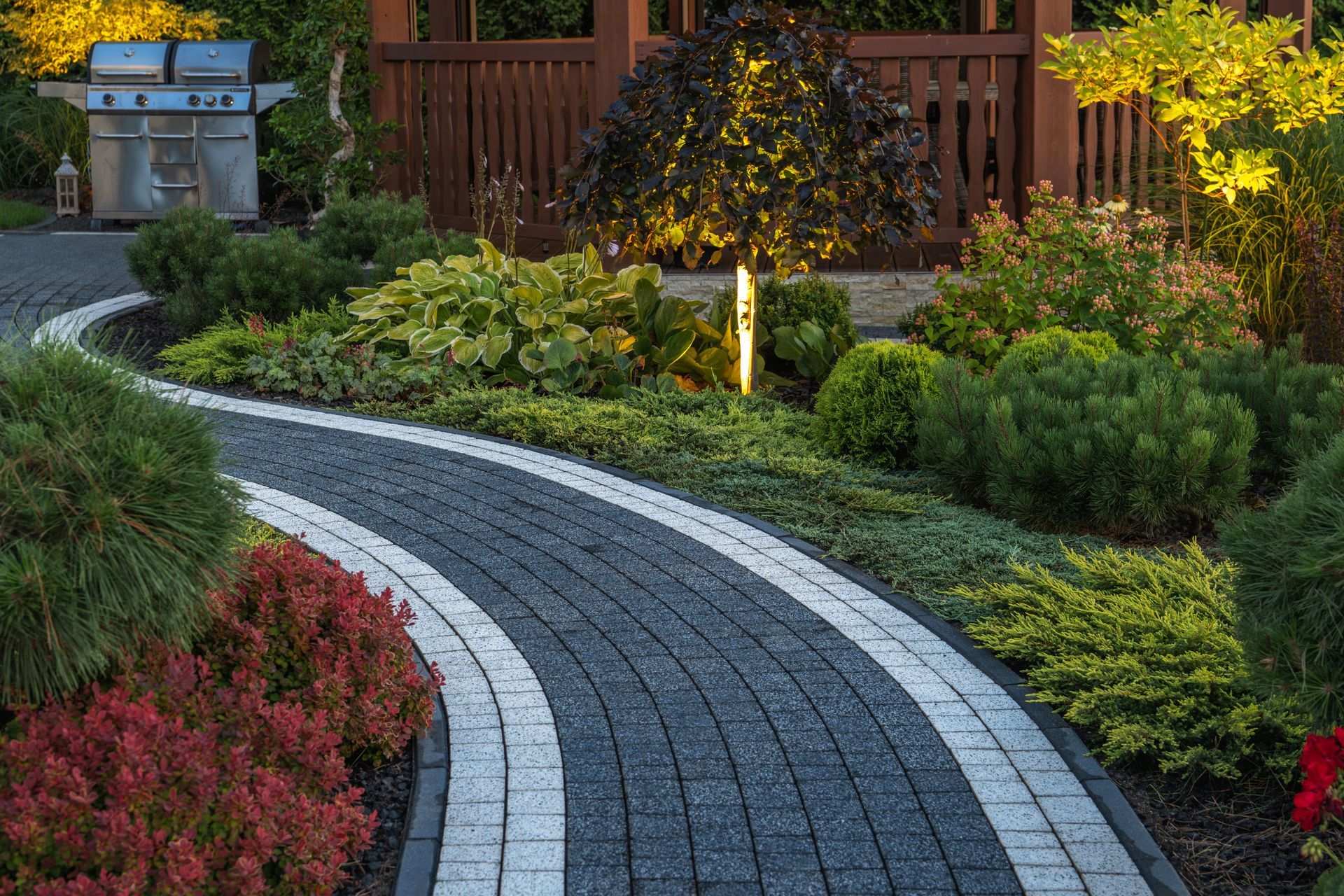 A brick walkway in a garden with a gazebo in the background.