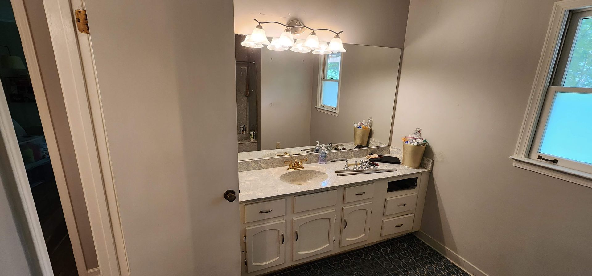 A bathroom with a sink , mirror , cabinets and a window.
