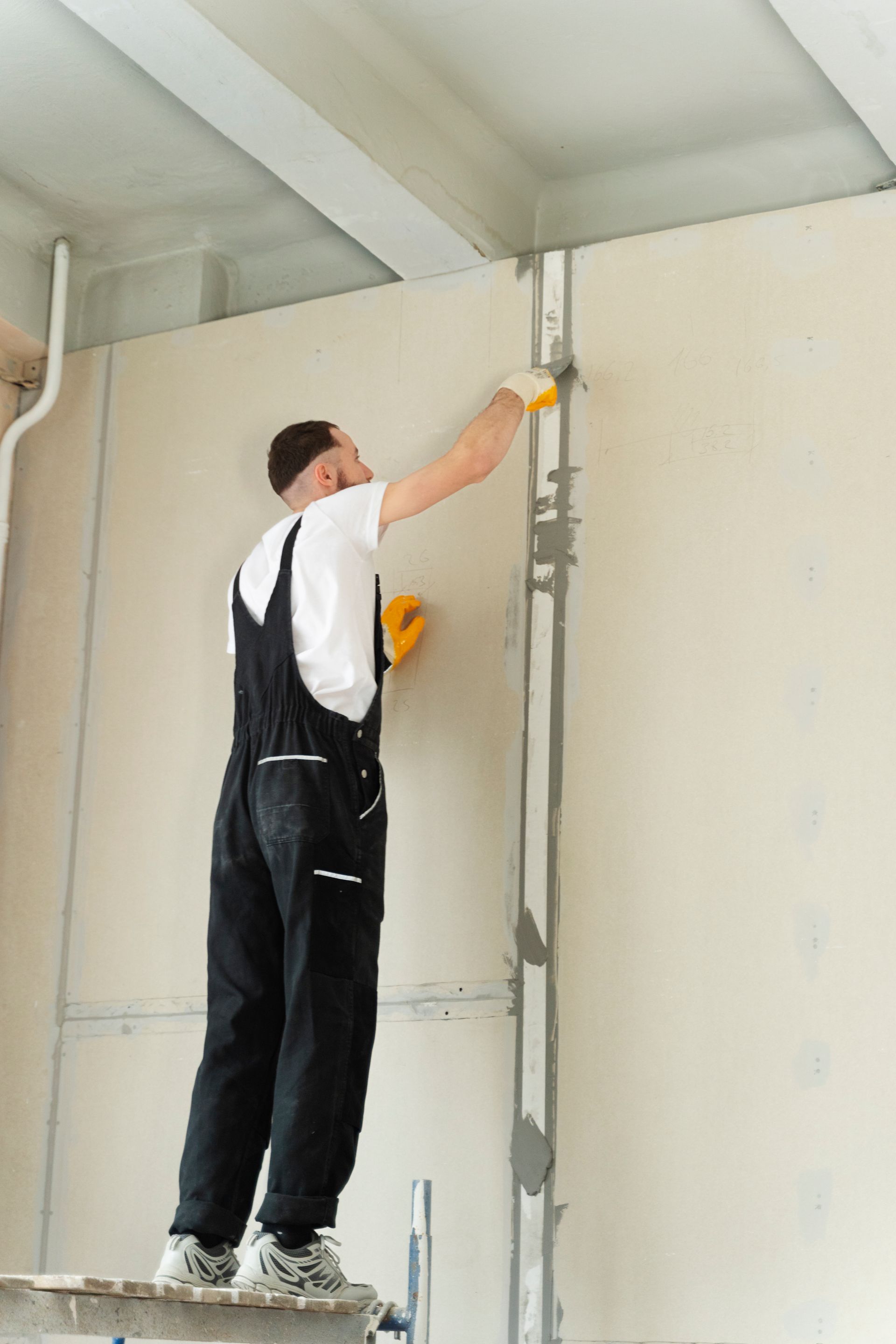 A man is standing on a scaffolding painting a wall.