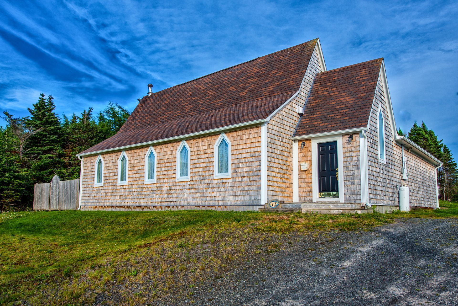 A small church with a red roof is sitting in the middle of a grassy field.