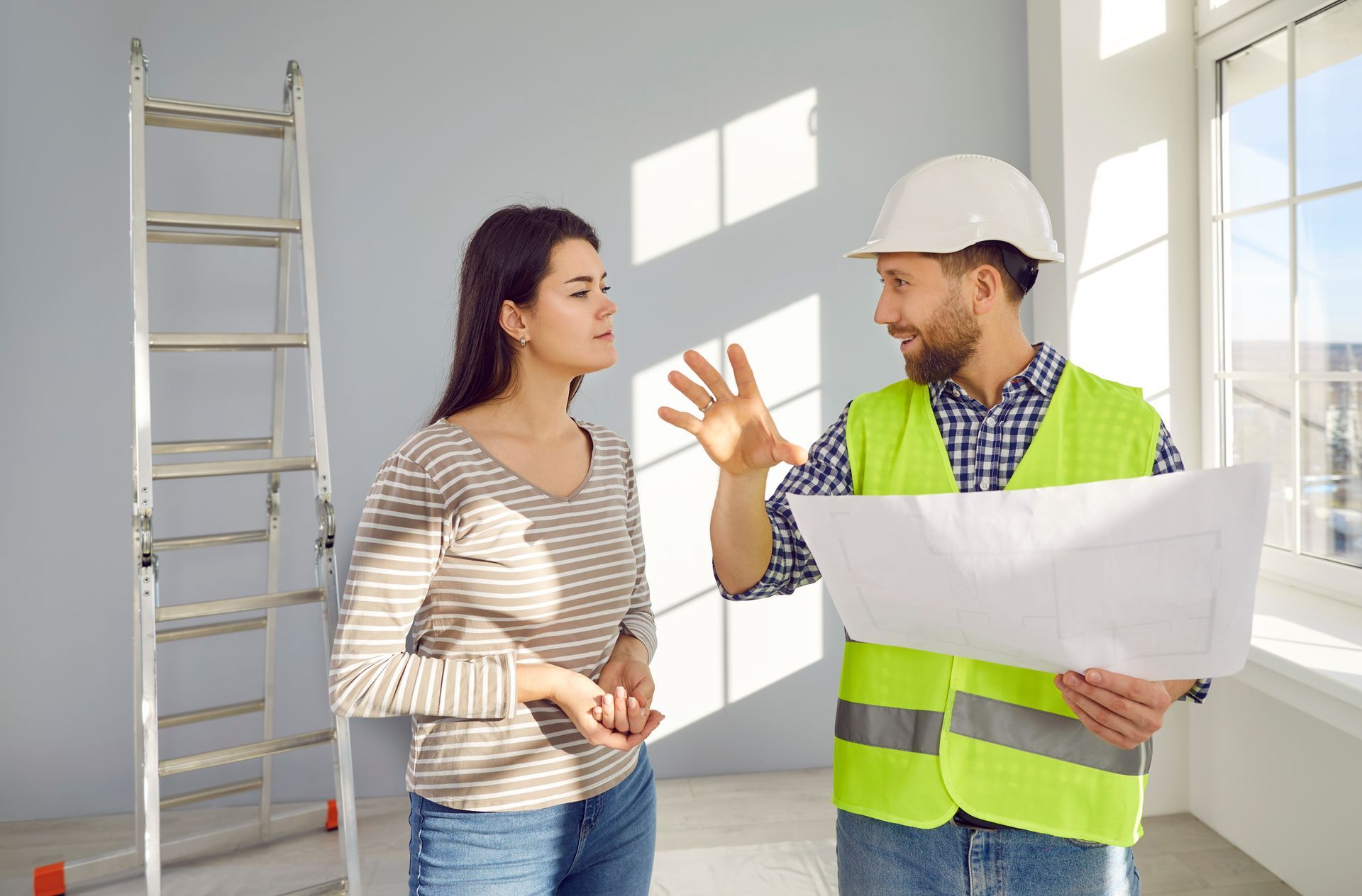 A man in a hard hat is talking to a woman while holding a blueprint.