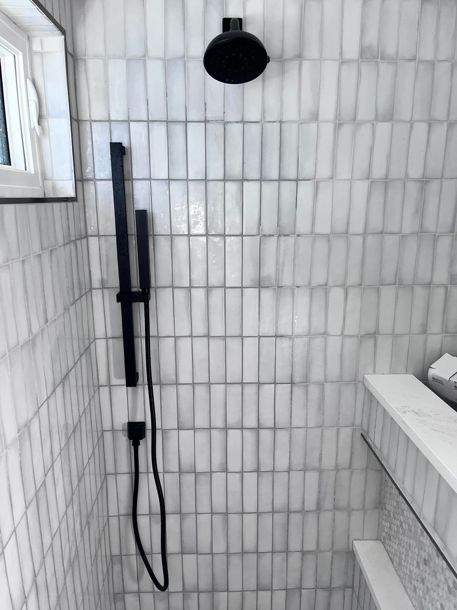 A shower with white tiles and a black shower head.