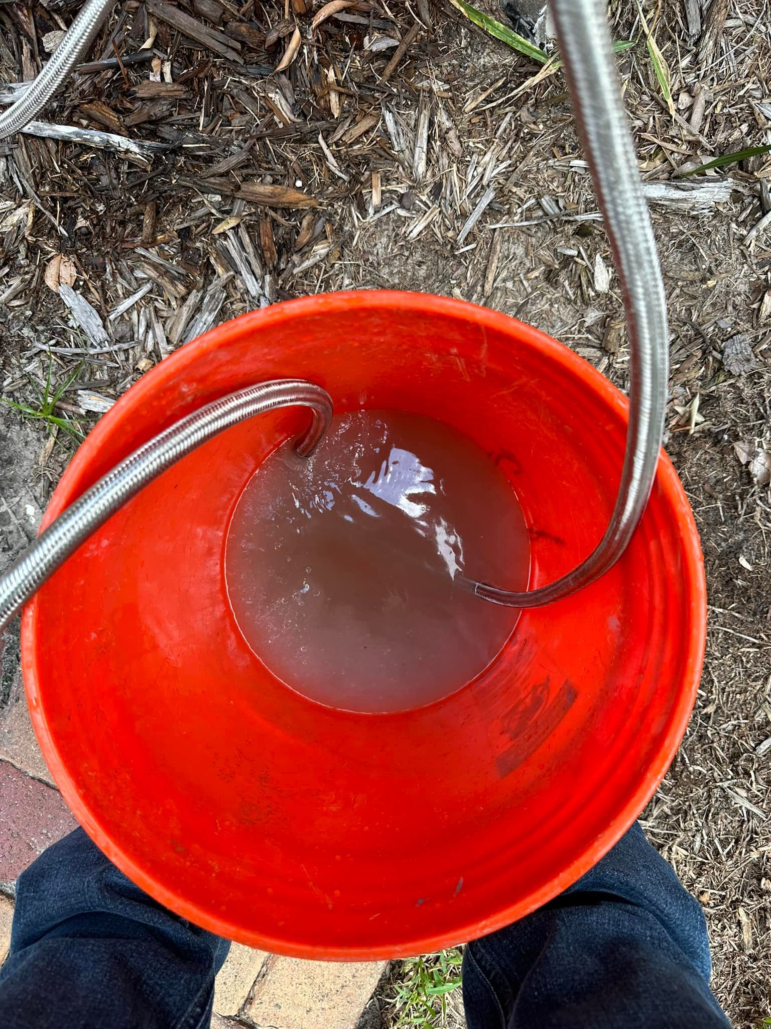 A person is standing next to a red bucket filled with water