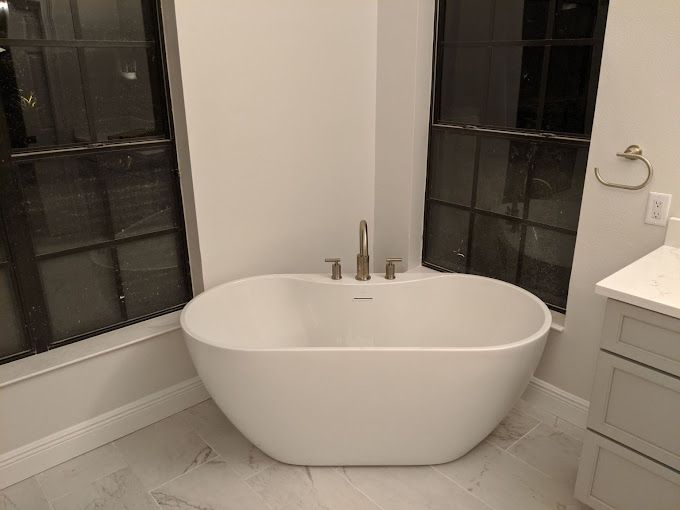 A white bathtub is sitting in the corner of a bathroom next to a window.