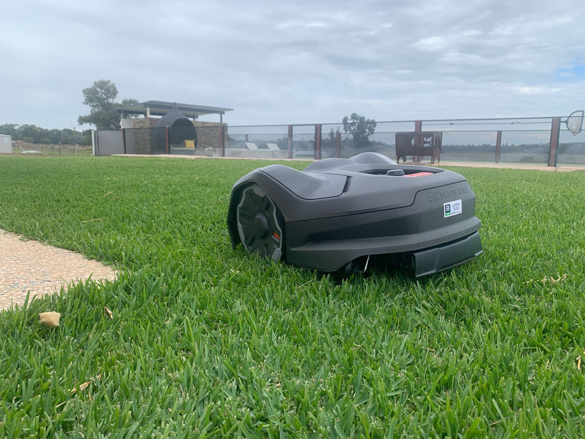 Robot lawn mower on a green lawn, background of a building and overcast sky— M.M & Mechanical in Dubbo, NSW